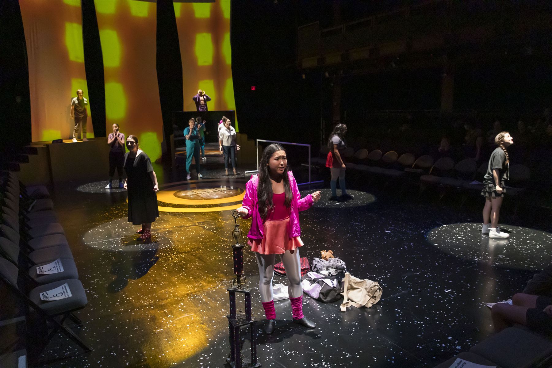 The full cast scattered across the stage in individual spotlights