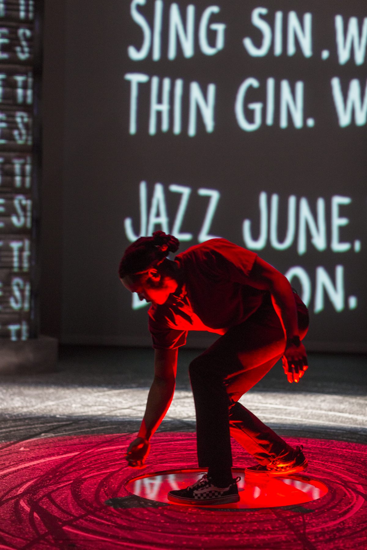 Brian Alexander Davis as Omari, crouched in red light before projected poetry, Pipeline