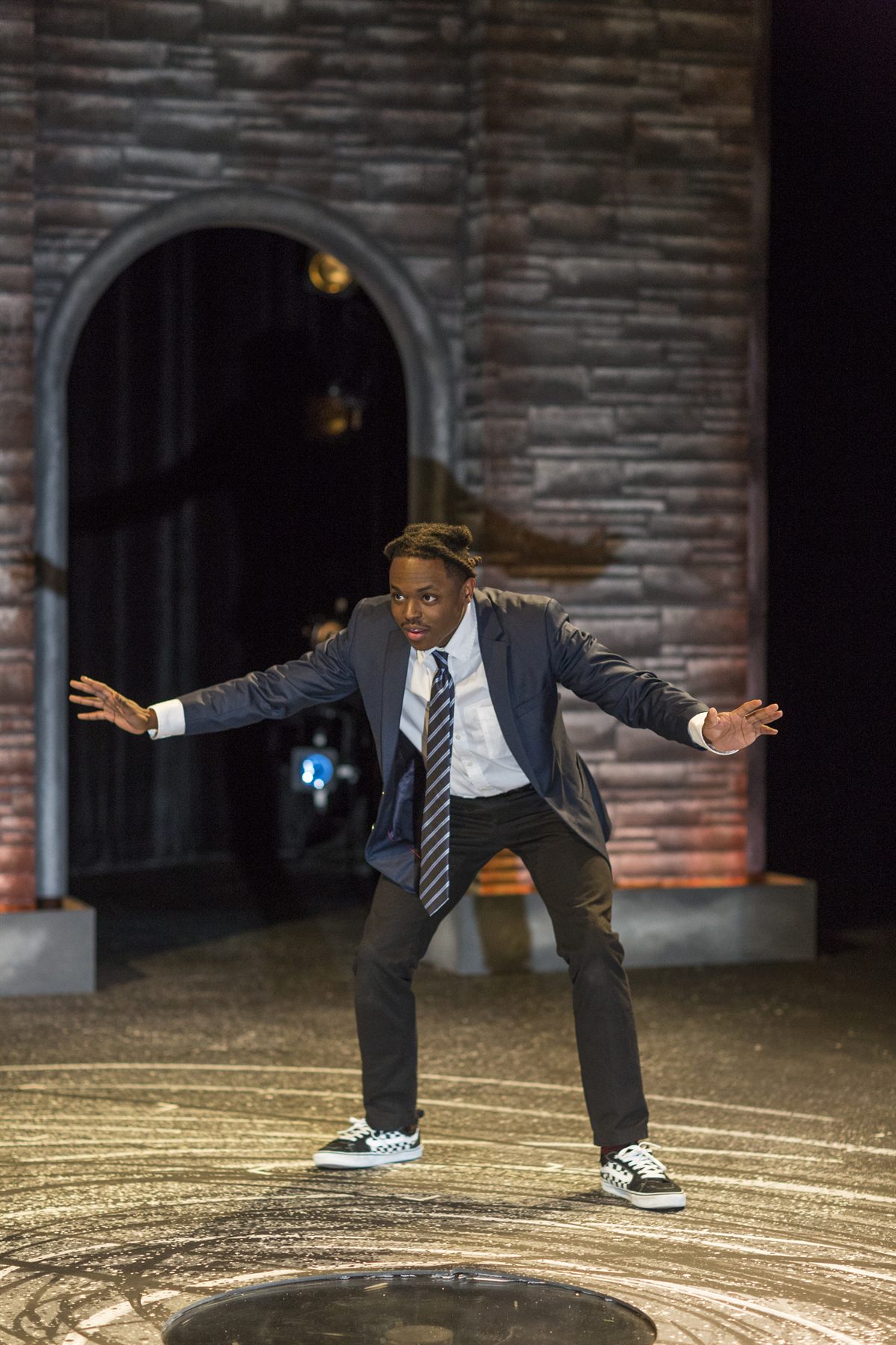 Omari in a school blazer and tie, arms spread mid-scene