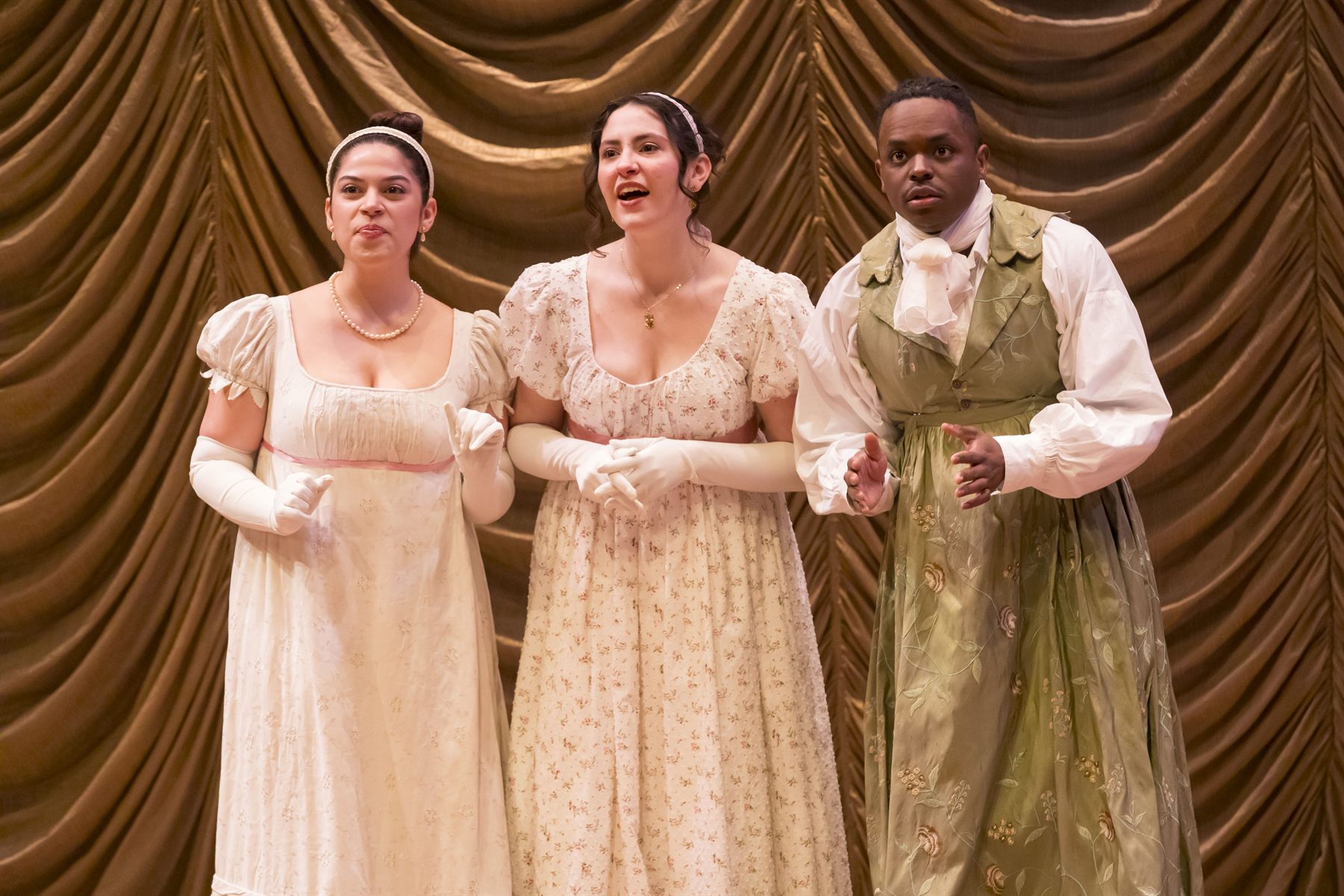 Three performers arm in arm before a gold curtain
