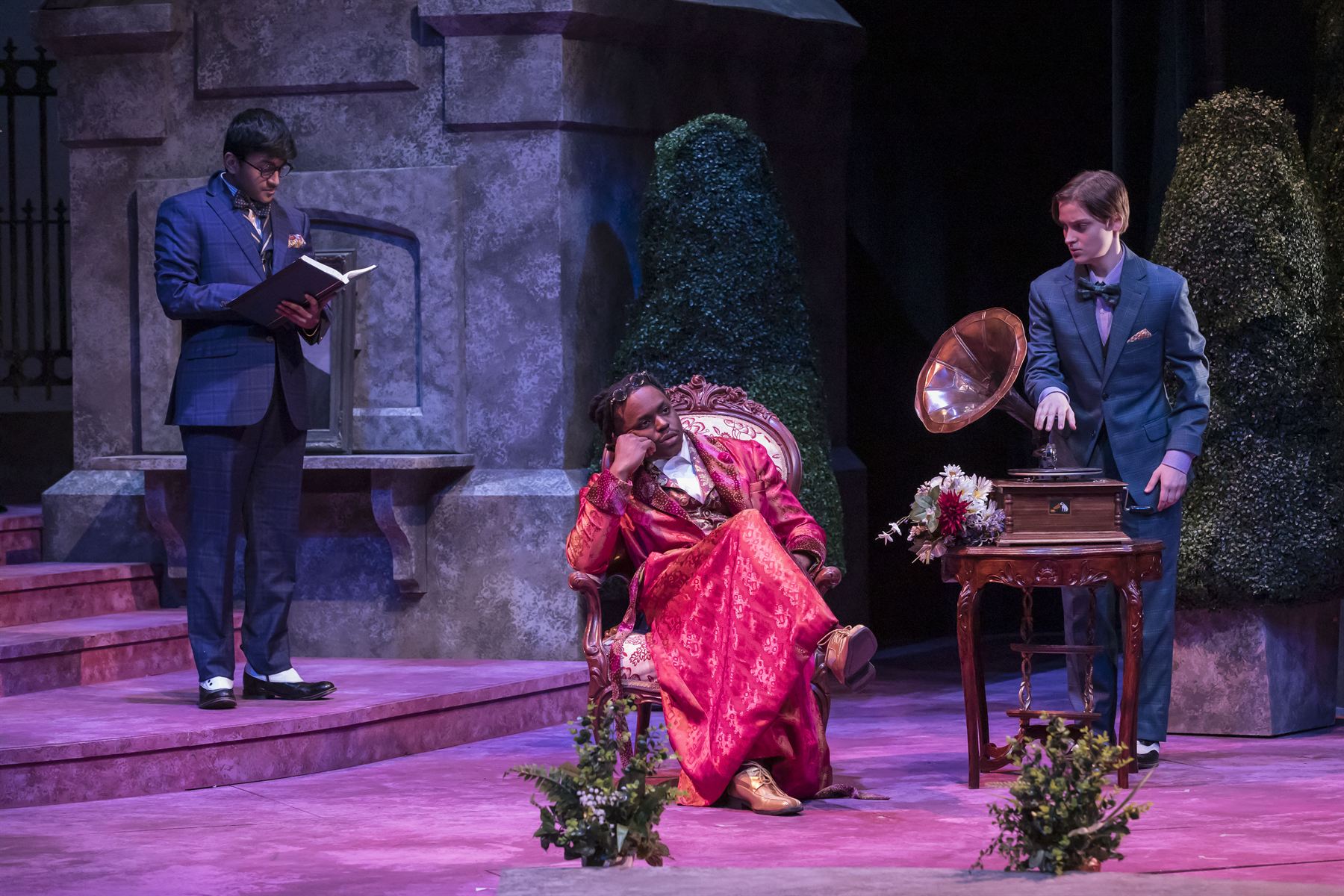 Orsino lounging in a red silk robe on an ornate chair, attendants and a gramophone nearby