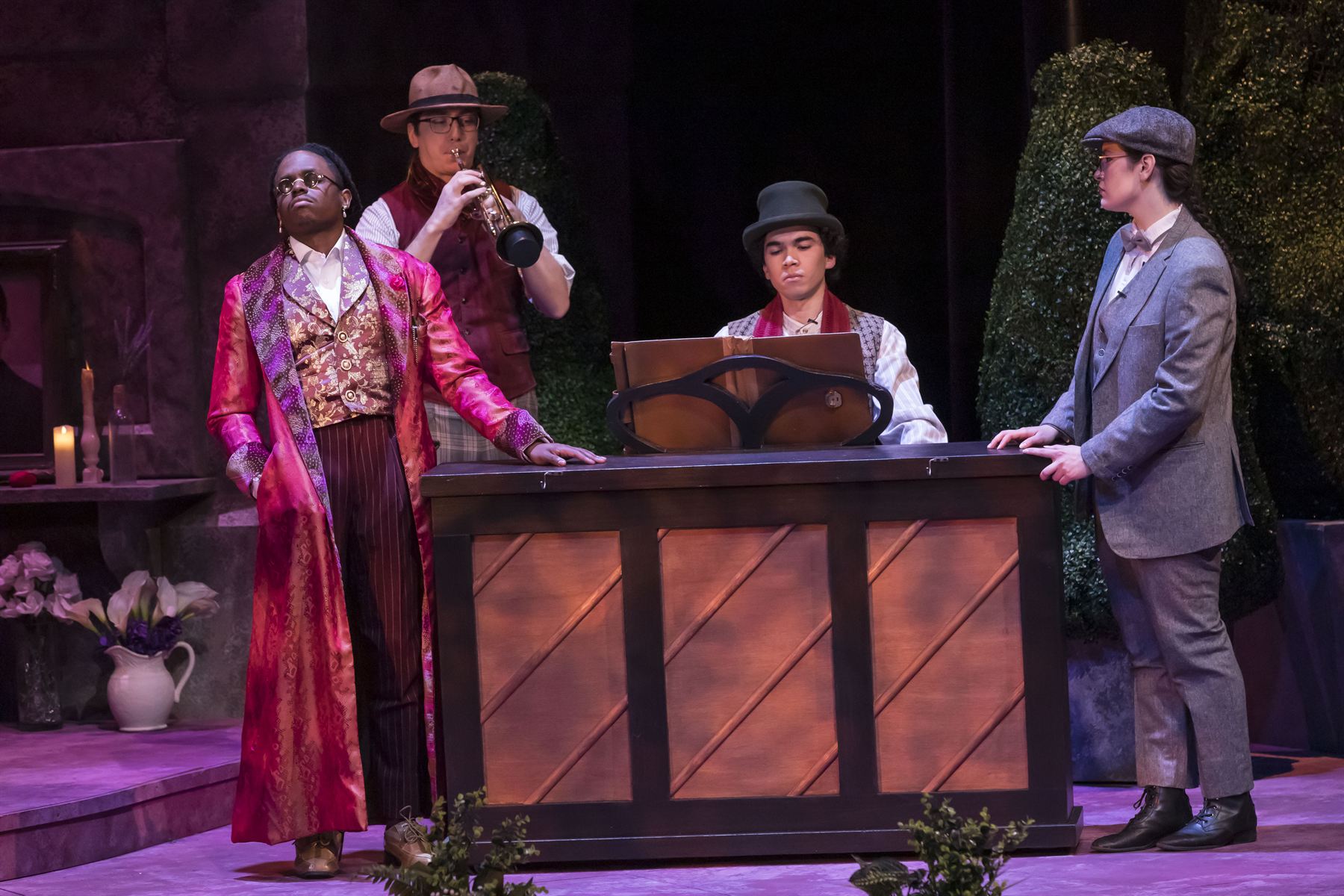 Orsino in a pink brocade robe beside musicians playing trumpet and piano